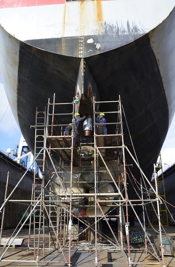 Mannen bezig met het roer van een schip in het droogdok